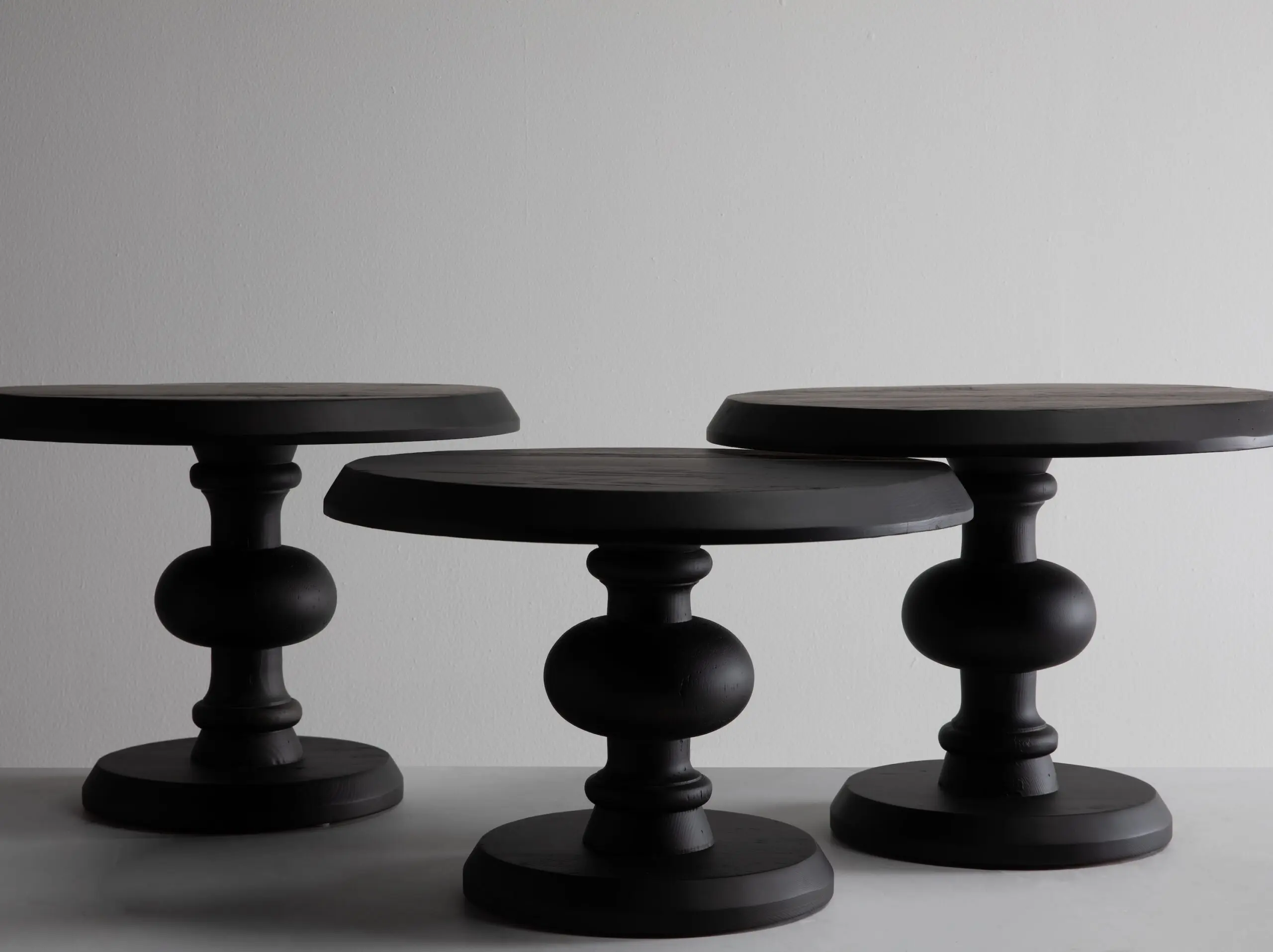 Close-up of black wooden chess pieces on a white tabletop against a plain gray wall.
