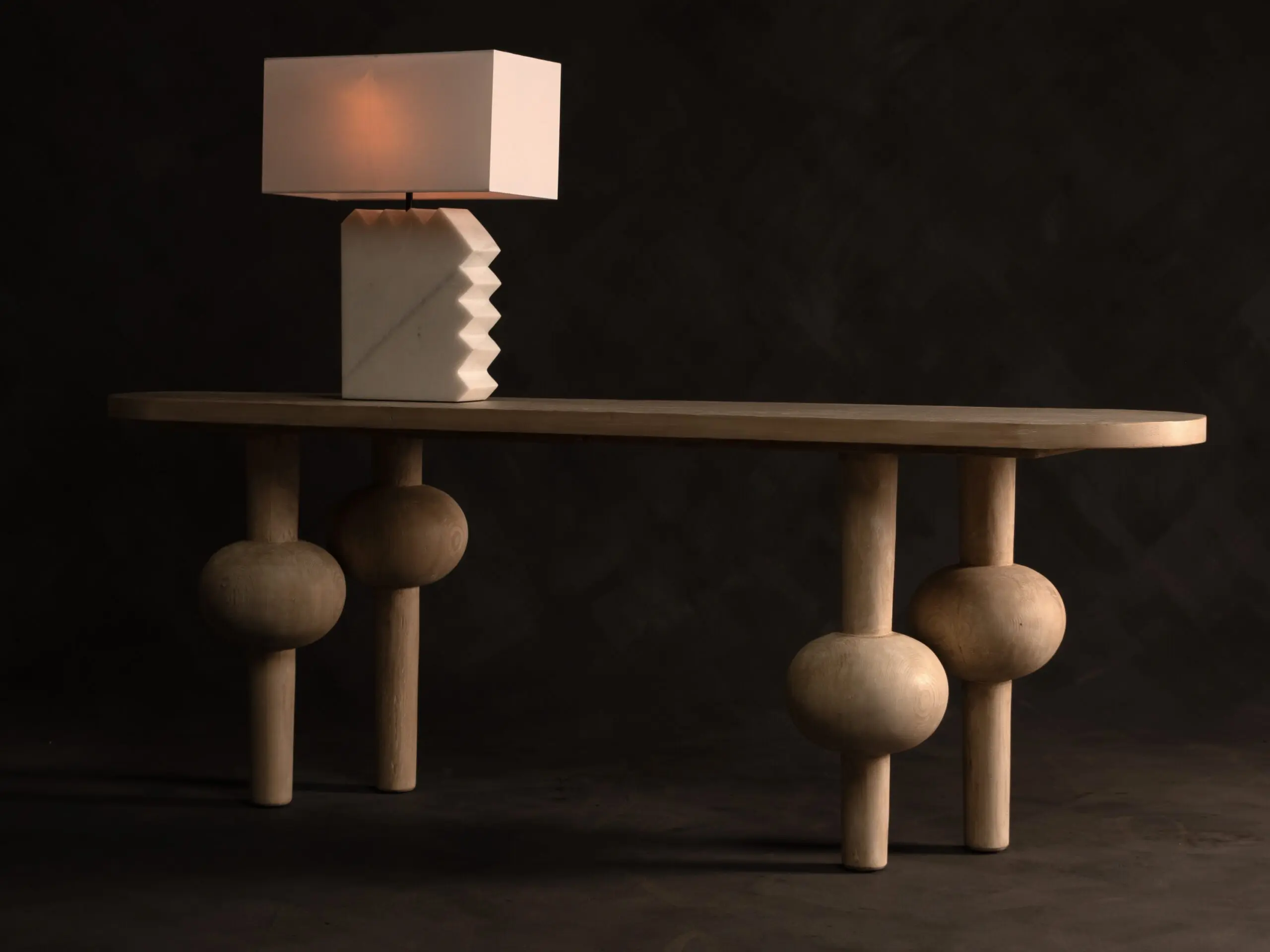 White rectangular lampshade on a white geometric base, placed on a wooden tabletop against a dark backdrop.